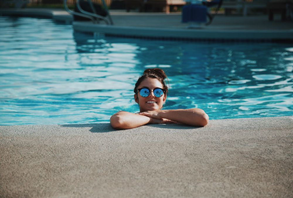 woman smiling and resting on the side of a pool deck