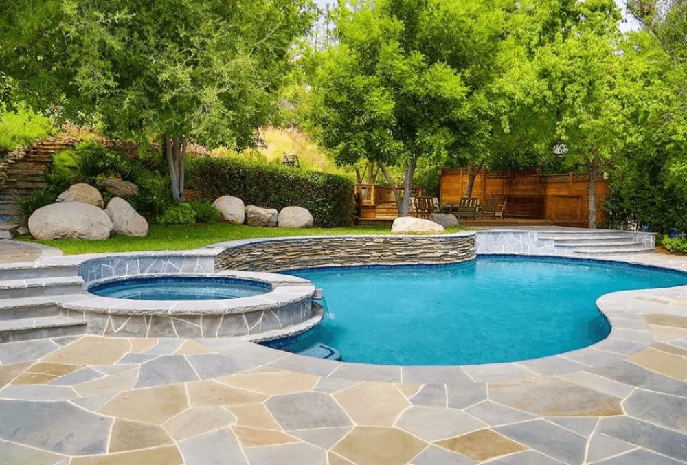 Modern stone pool deck with lush backyard